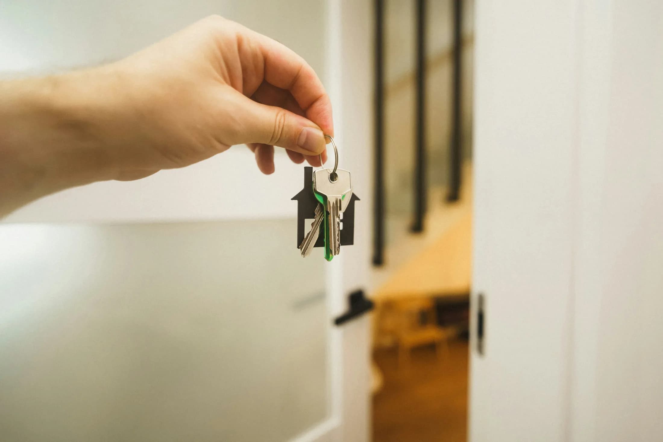 Eine Hand hält Wohnungsschlüssel vor einer geöffneten Tür